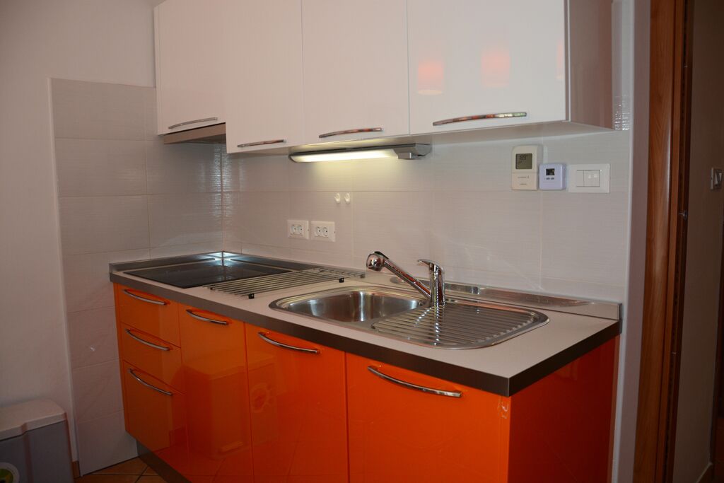 A kitchen with two sinks, orange cabinets, and a white backsplash.