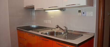 A kitchen with two sinks, orange cabinets, and a white backsplash.