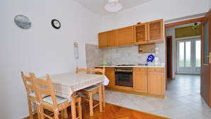 Uma cozinha com armários de madeira, uma mesa de jantar com cadeiras, um relógio e piso ladrilhado.