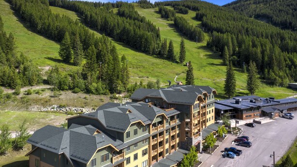 A multi-story hotel with a ski resort view, featuring a parking lot and a mountainous backdrop. - Top floor ski condo with direct ski in and out. Hiking and biking too! Hot tub (Whitefish)