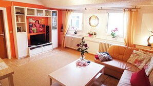 A living room with a white coffee table, orange sofa, and a TV on a stand. - Living Above The Roofs Of Cochem (Cochem)