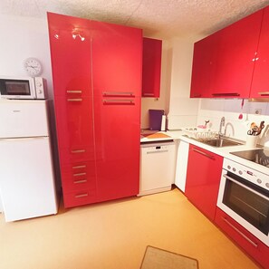 A kitchen with red cabinets, a white refrigerator, a microwave, a dishwasher, and a stove. - Living Above The Roofs Of Cochem (Cochem)