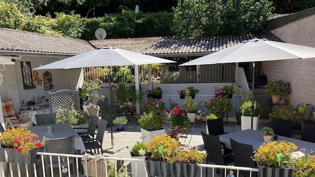 An outdoor patio area with tables and chairs, surrounded by potted plants and umbrellas. - Living Above The Roofs Of Cochem (Cochem)