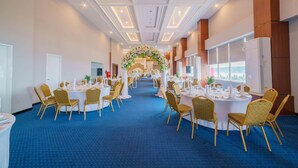A hotel ballroom with round tables, gold chairs, and a floral archway.