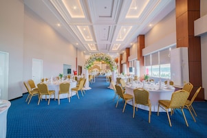 A hotel ballroom with round tables, gold chairs, and a floral archway.