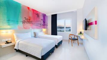 Habitación de hotel con dos camas, un escritorio con silla, televisor y ventana grande con vista.