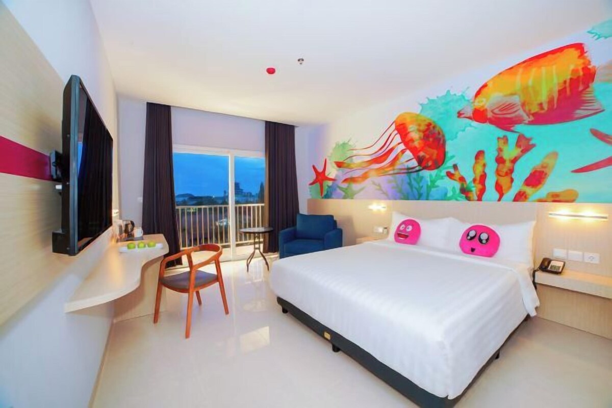 A hotel room with a large bed, a desk, a chair, a TV, and a mural of fish on the wall.