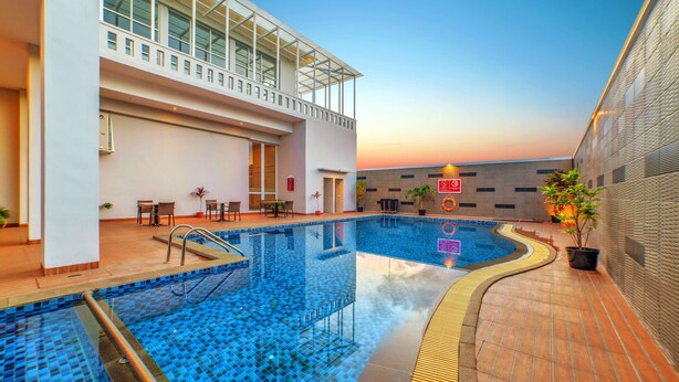 An indoor swimming pool with a glass ceiling, tiled flooring, and a seating area with tables and chairs.