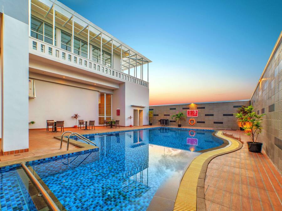 An indoor swimming pool with a glass ceiling, tiled flooring, and a seating area with tables and chairs.