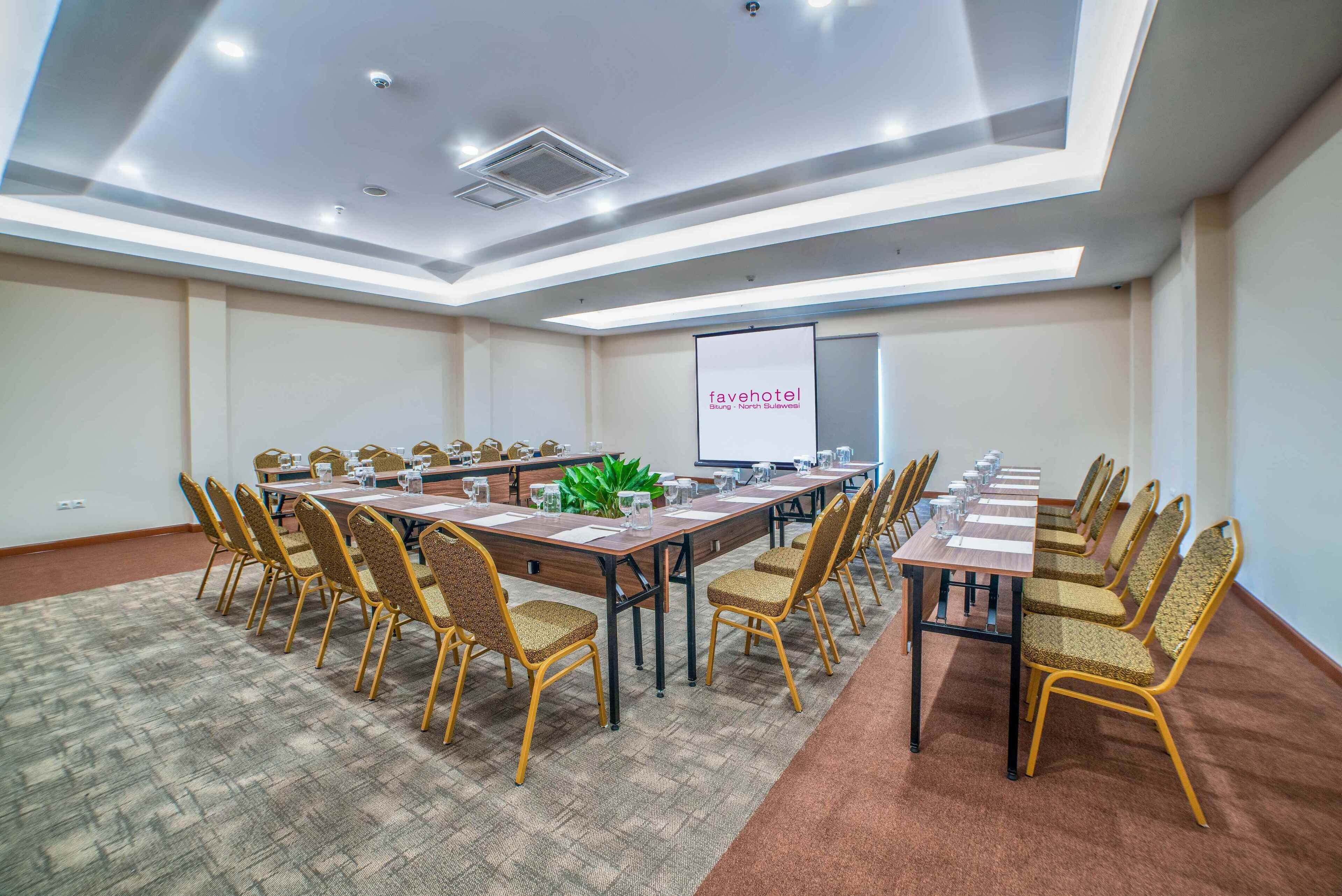 A conference room with a long table, chairs, a projector screen, and a carpeted floor.