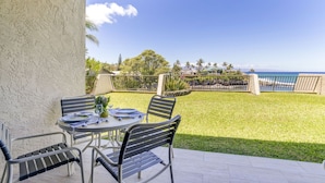 A patio with a table set for two, overlooking a grassy area and the ocean.