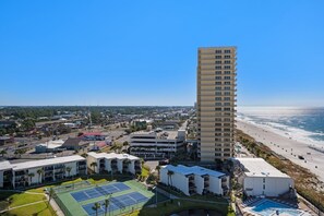 A high-rise hotel with a tennis court and pool area, overlooking a beach.