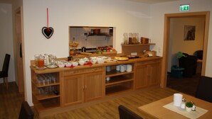 A kitchen with wooden cabinets, a countertop with various food items, and a heart-shaped decoration on the wall. - Hotel Garni Dorfblick (Sankt Anton am Arlberg)