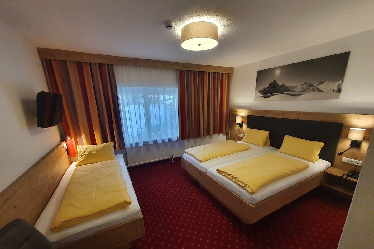 Camera d'albergo con due letti, un'ampia finestra con tende e un quadro appeso, oltre a un tappeto rosso.