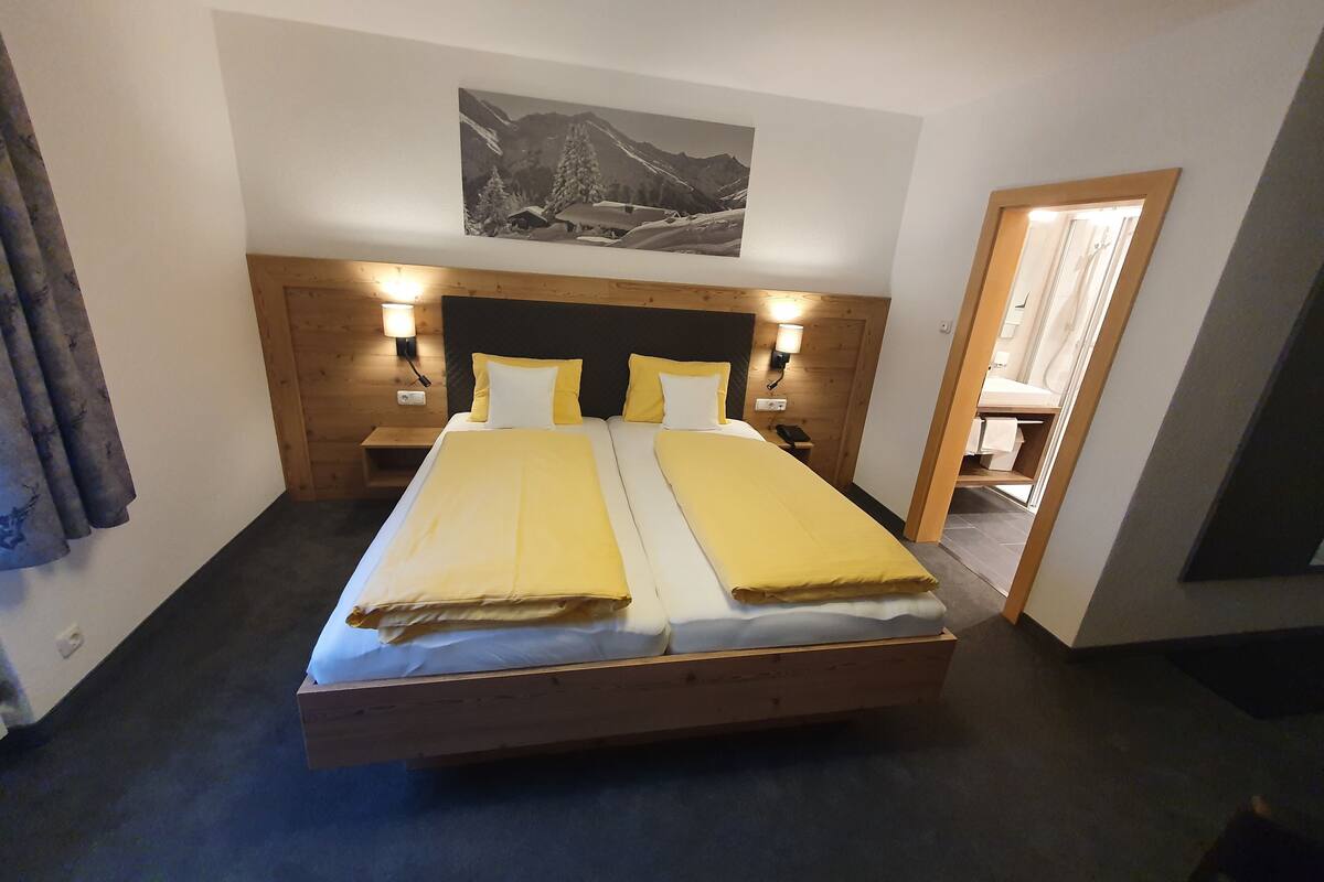 Un letto matrimoniale con una testiera in legno, due comodini con lampade e un quadro raffigurante un paesaggio montano sopra il letto.