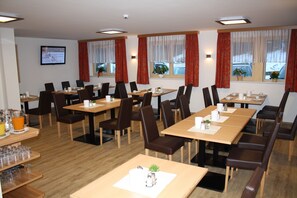 Ein Hotelrestaurant mit mehreren Tischen und Stühlen, einem Fernseher an der Wand und Fenstern mit Vorhängen.