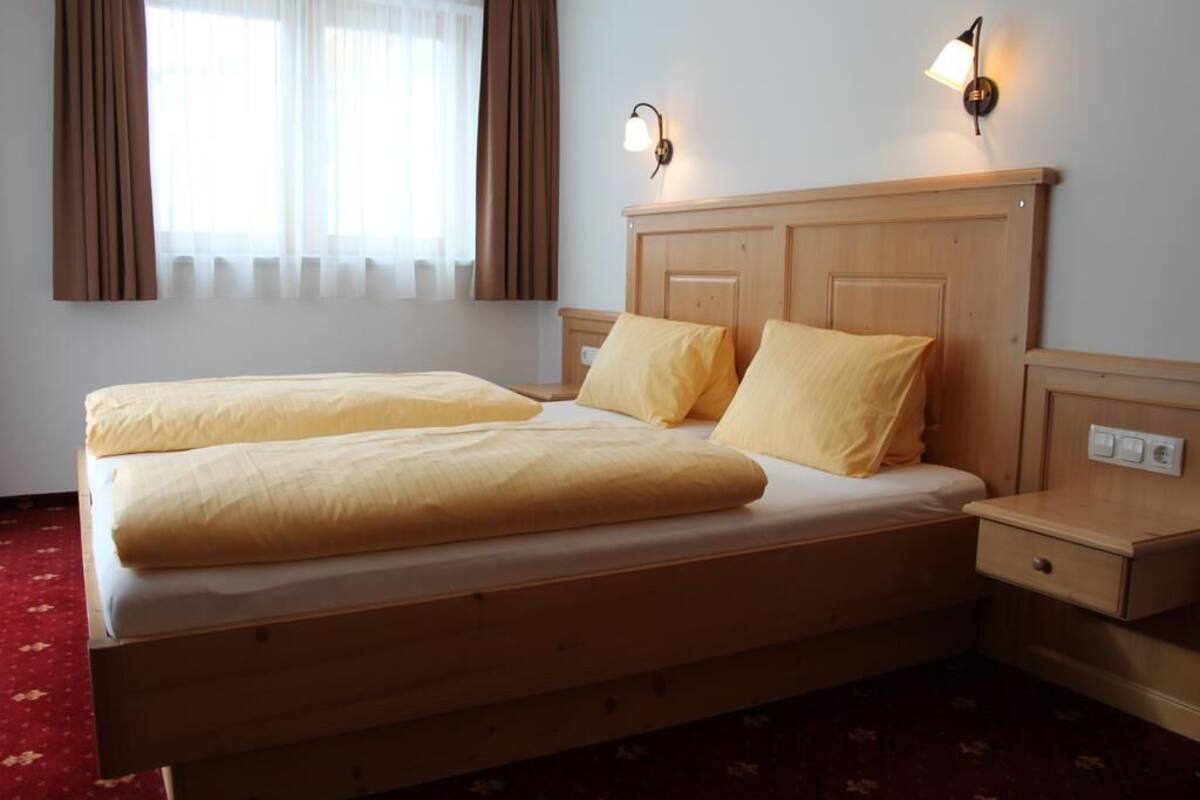 Un letto matrimoniale con testiera in legno, due abat-jour e un comodino con cassetto.
