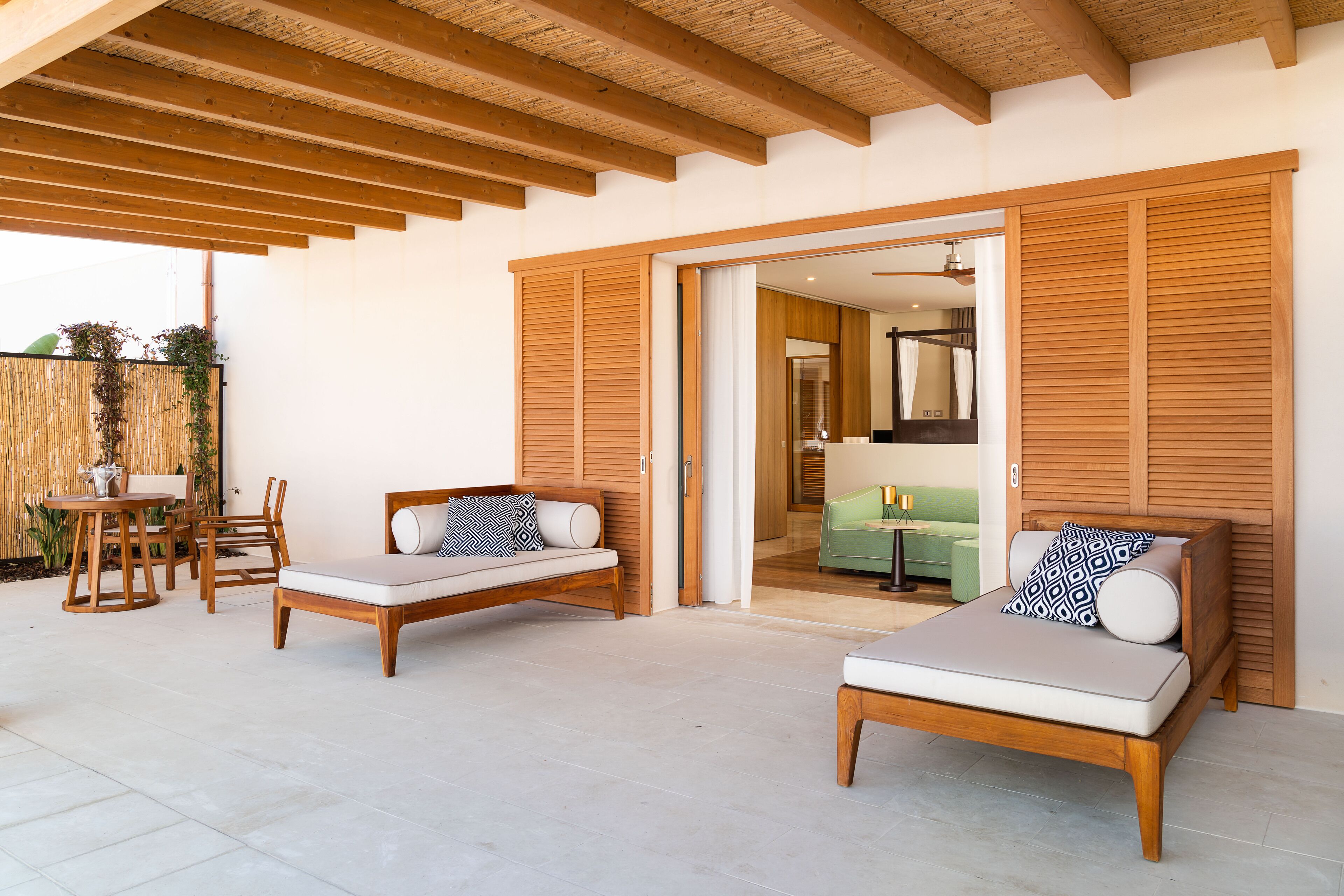 A patio area with two wooden lounge chairs, a small table, and a wooden ceiling structure.
