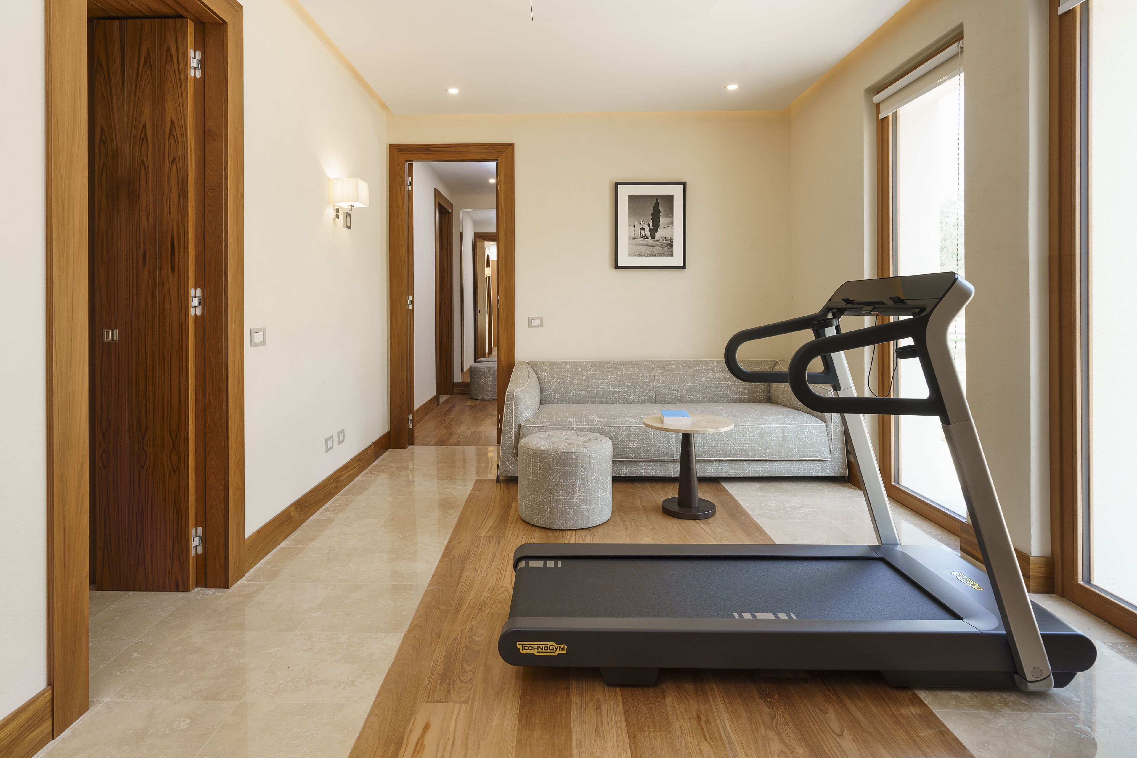 Una sala de estar moderna con una caminadora, un sofá gris y una pequeña mesa redonda.