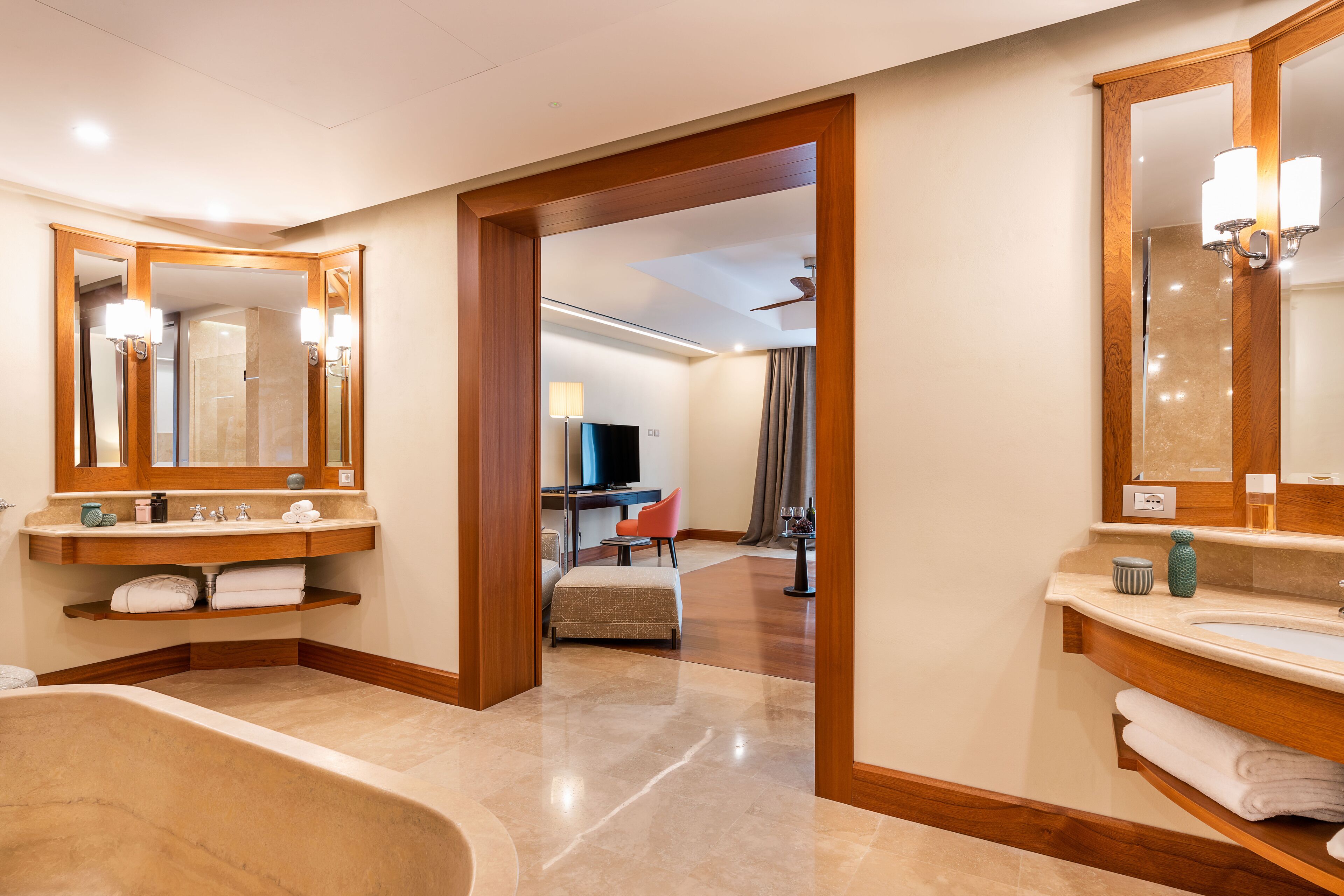 Une salle de bain moderne avec une grande baignoire, deux lavabos et un espace coiffeuse. On trouve également un téléviseur dans la pièce adjacente.