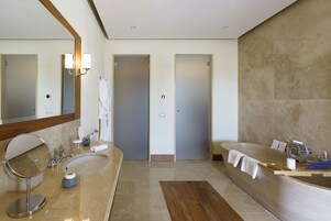A modern bathroom with dual sinks, a large bathtub, and a mirror with wall-mounted lights.