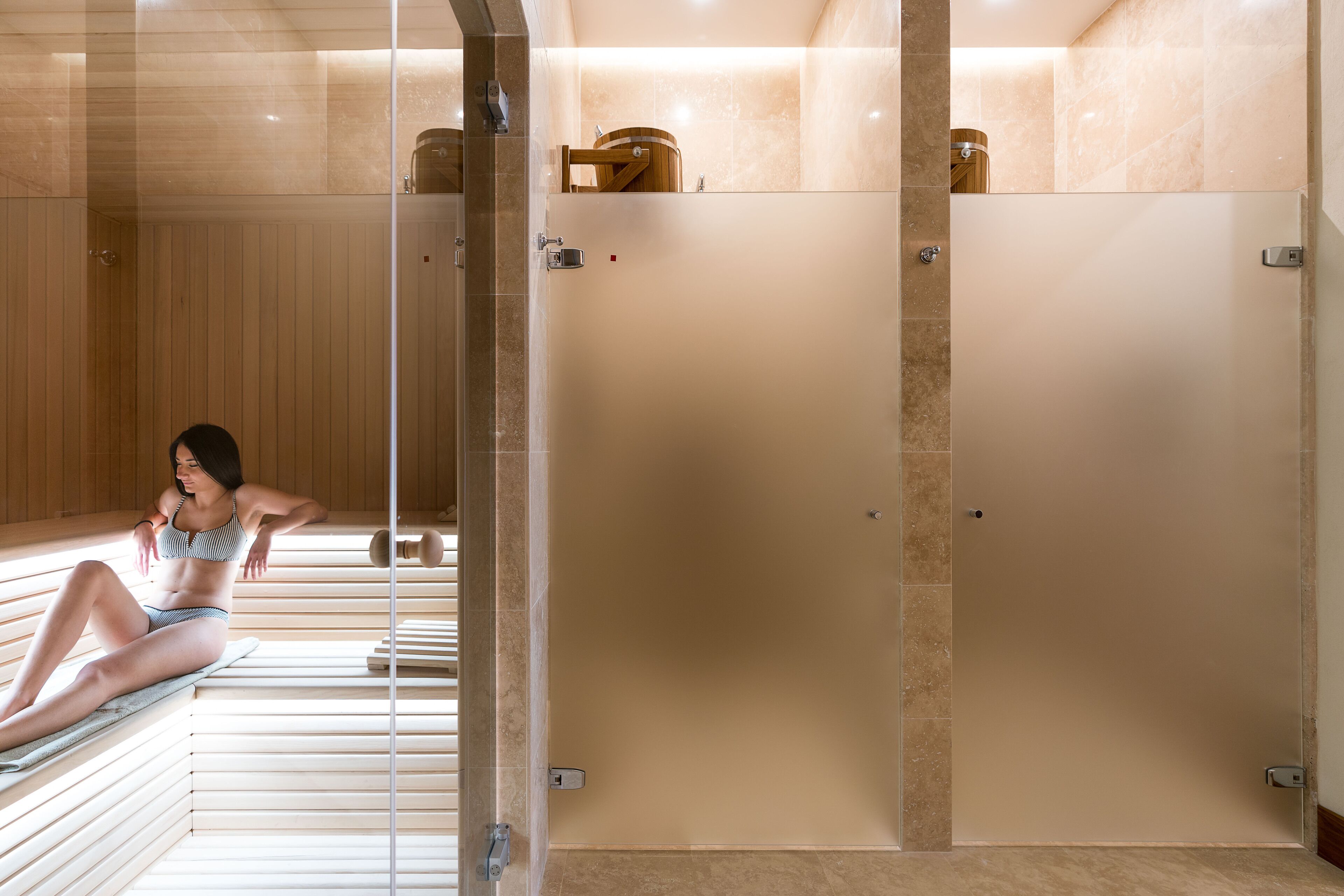 Una sala de sauna con bancos de madera y un panel de vidrio.