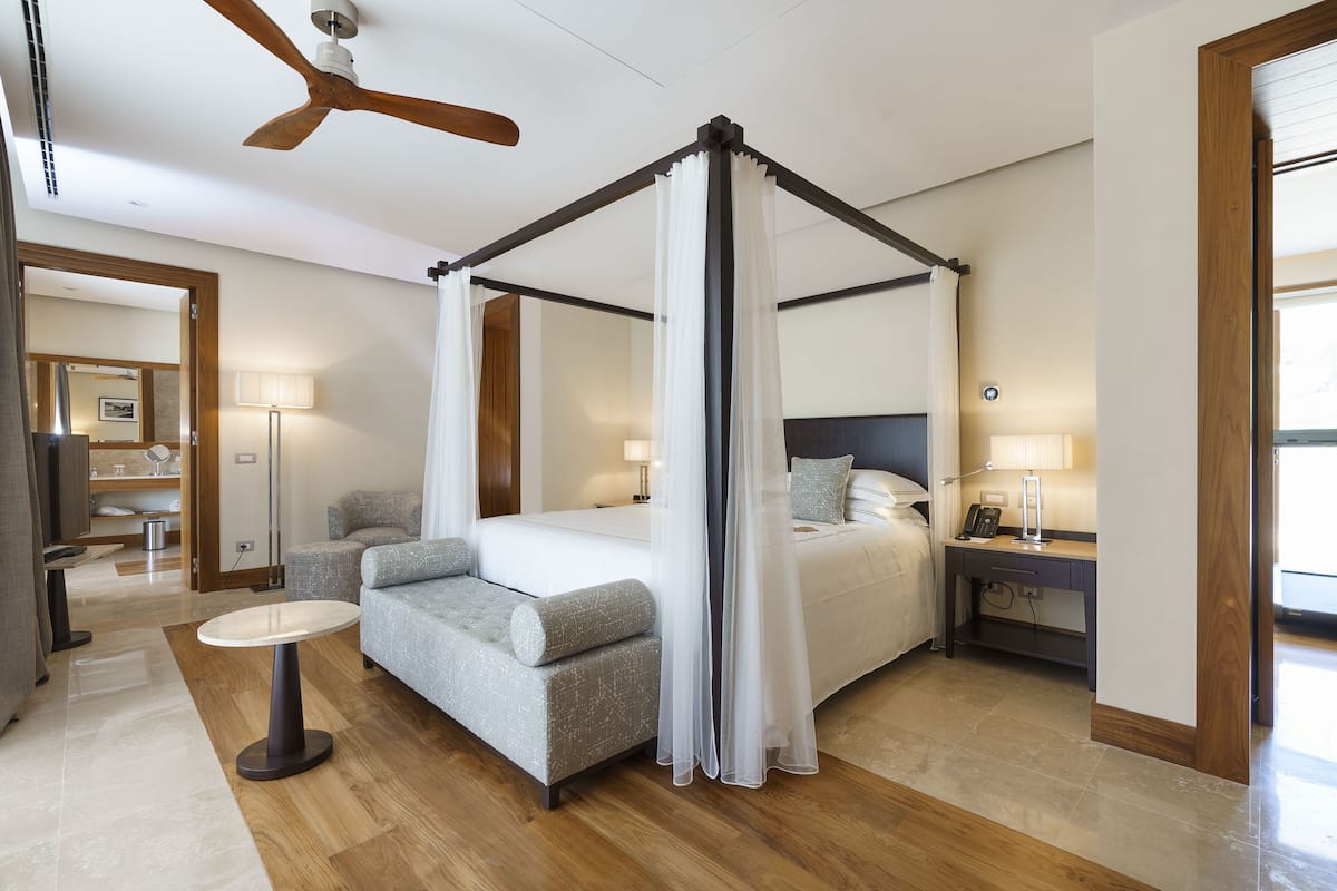 A four-poster canopy bed with a nightstand, a sofa, and a small table in a modern hotel room.