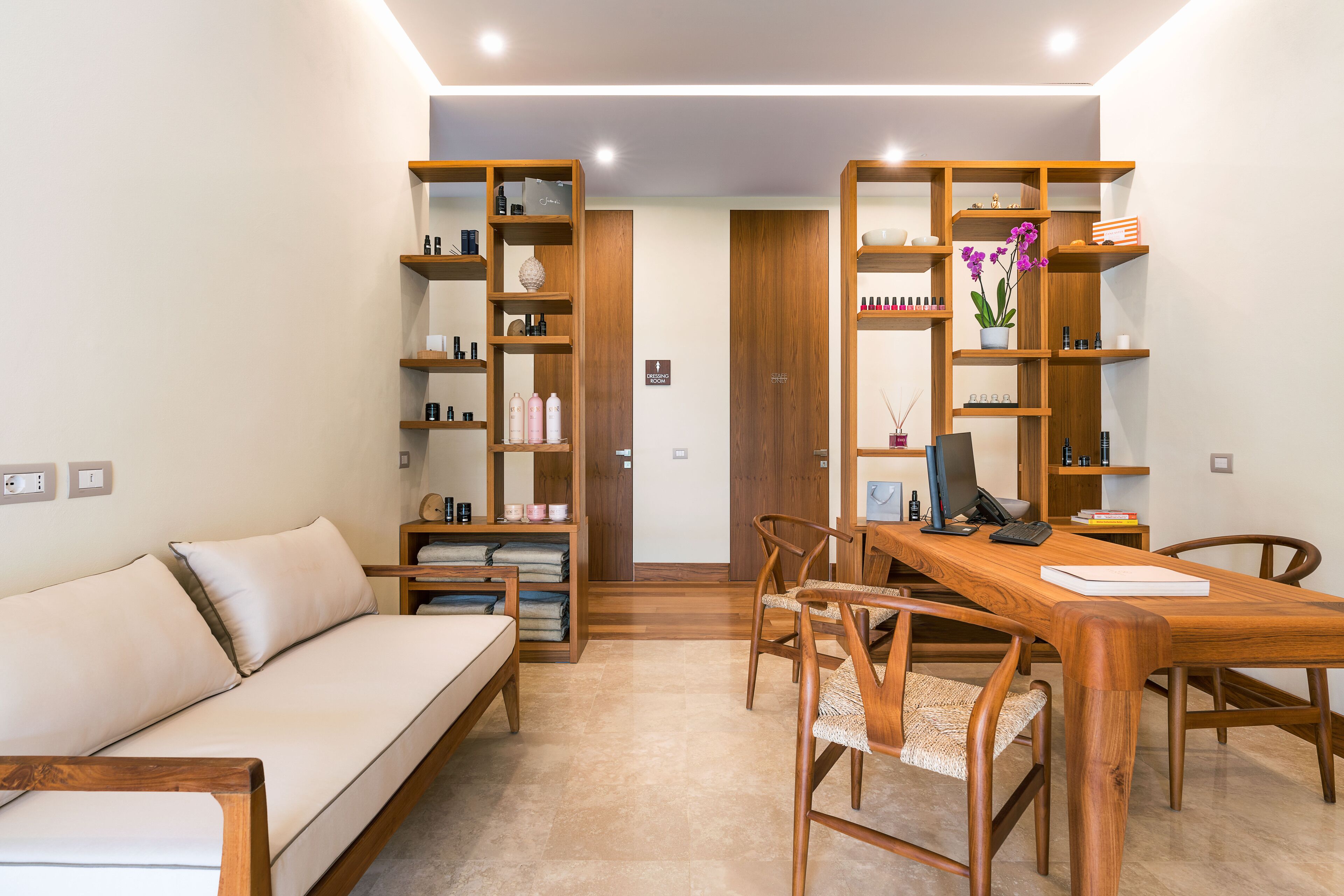 A modern living room with a sofa, wooden dining table, chairs, and built-in wooden shelving with various items.