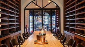 A wine cellar with a long wooden table and chairs, surrounded by shelves of wine bottles.