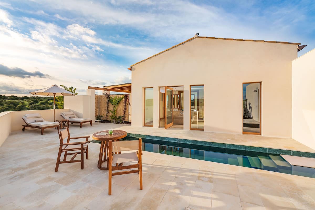 A modern outdoor pool area with lounge chairs and a table, surrounded by a white building with large glass doors.