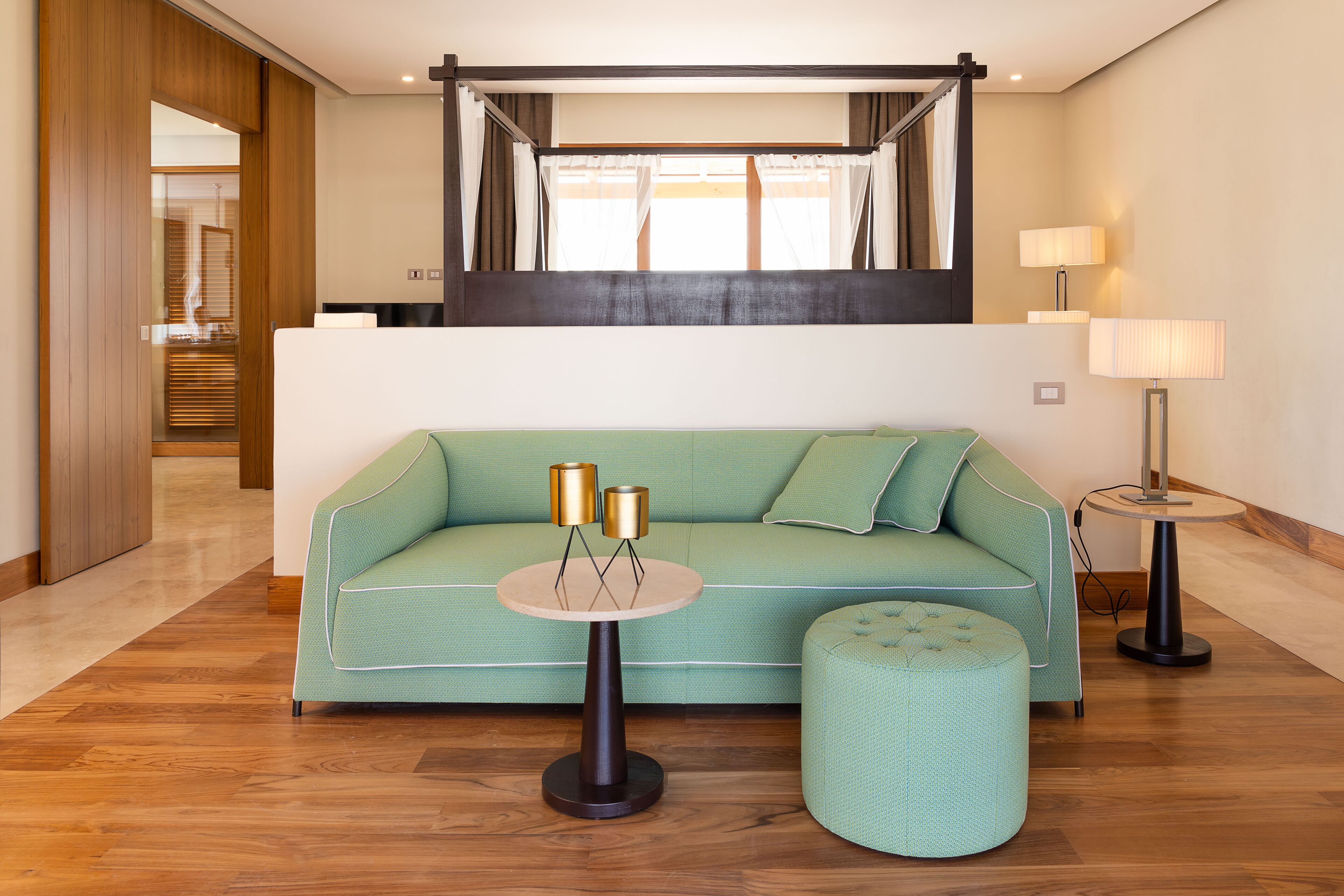 A modern living room with a green sofa, a round table with two lamps, and a matching ottoman.
