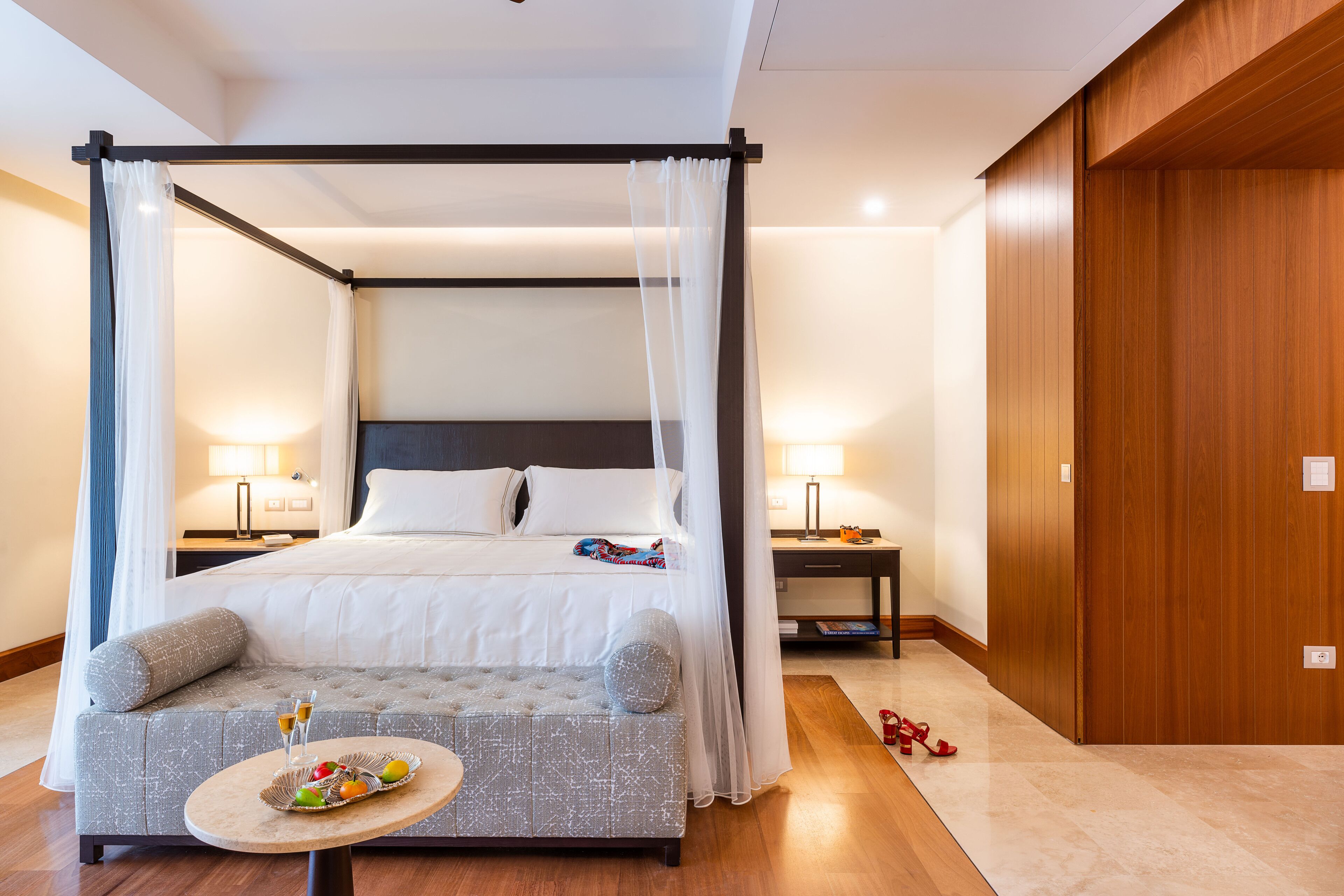 Ein Hotelzimmer mit Himmelbett, einer Couch, einem kleinen Tisch mit Früchten und Getränken sowie einem Holzschrank.
