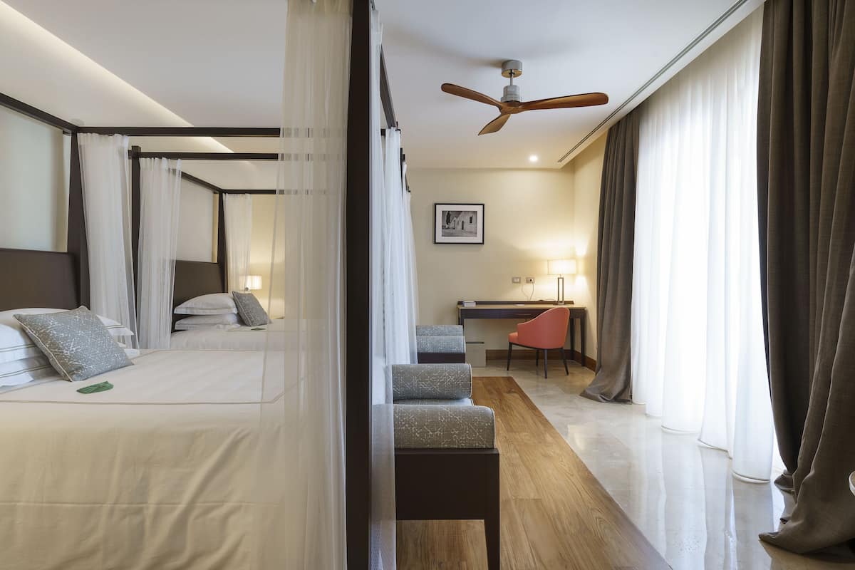 A hotel room with a bed, a desk, a chair, and a ceiling fan.