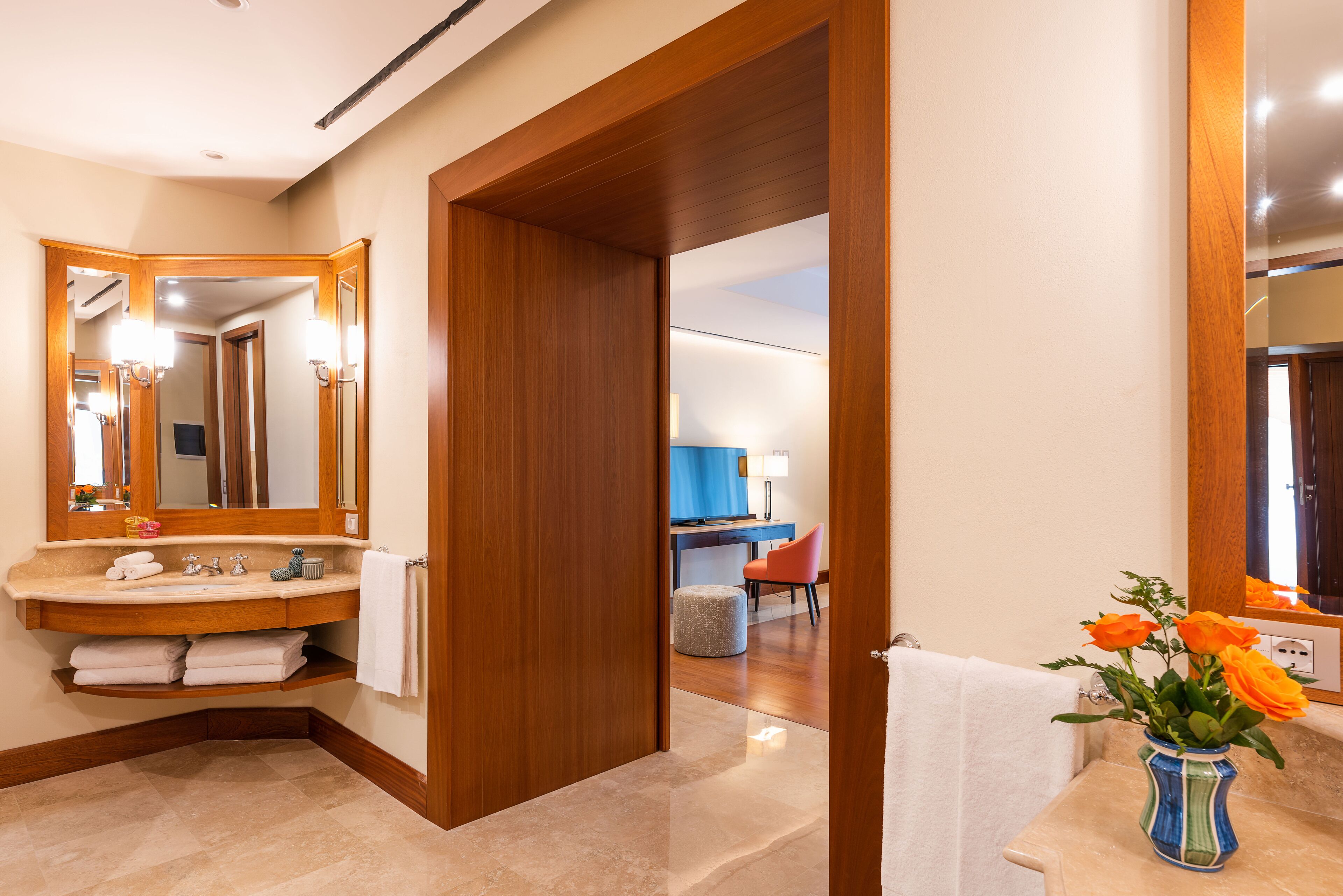 A modern bathroom with a wooden vanity, a large mirror, and a vase of flowers.
