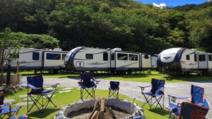 Vários trailers de viagem estacionados em um camping, com área de estar externa e lareira.