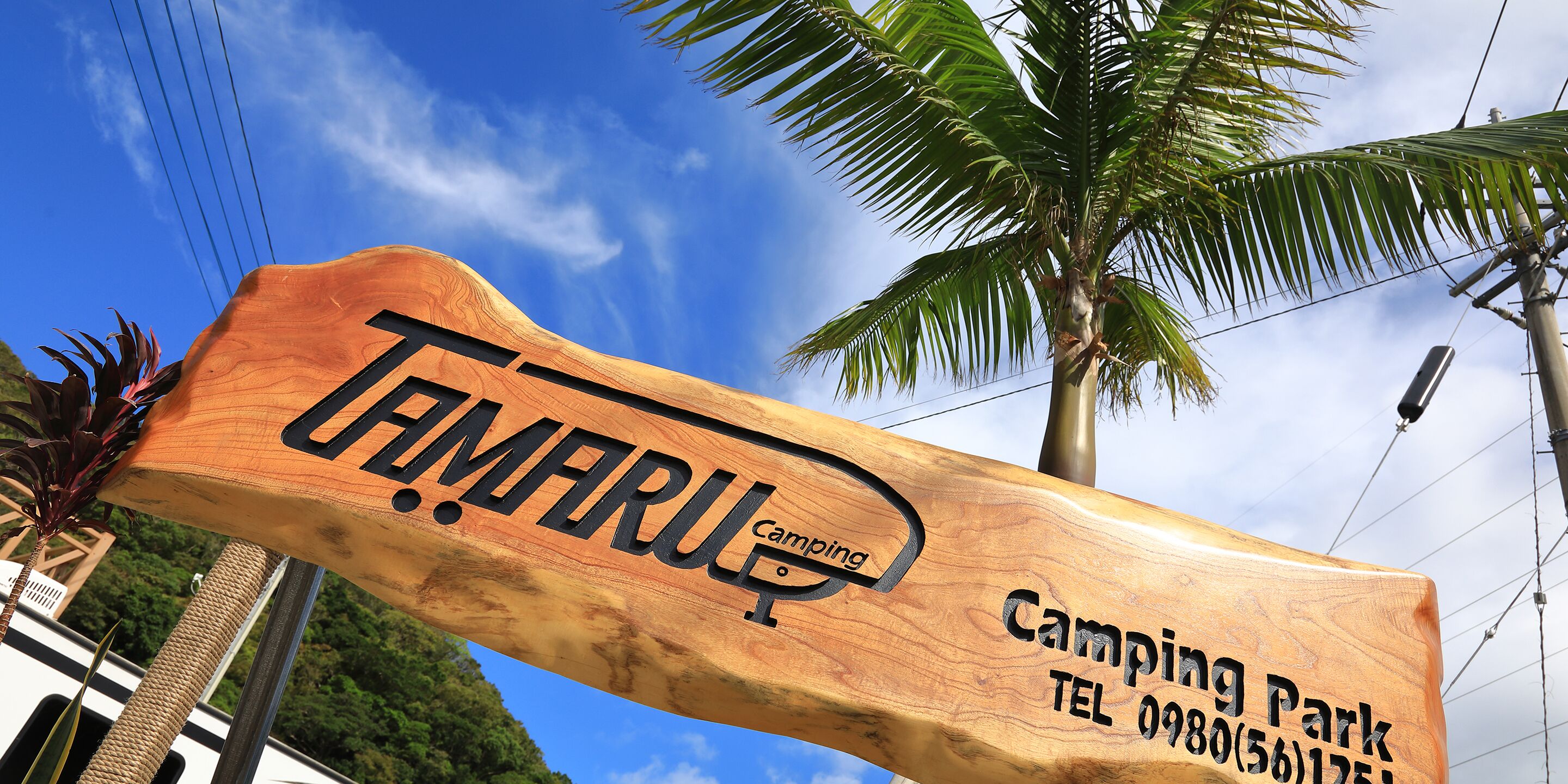 A wooden sign for Tamaru Camping Park with contact information.