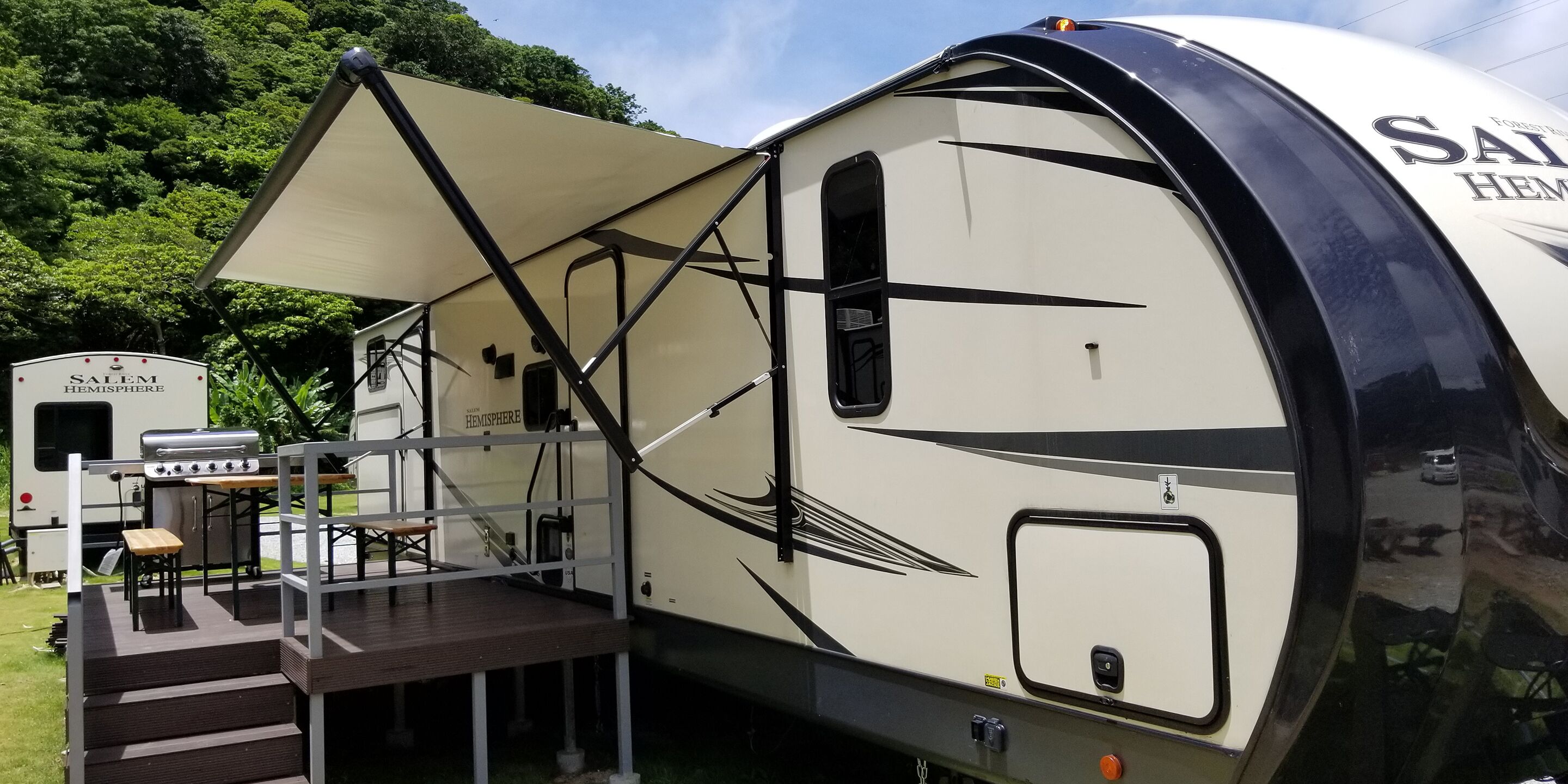 A recreational vehicle with a covered deck, a grill, and a small table.