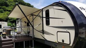 A recreational vehicle with a covered deck, a grill, and a small table.