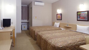 Ein Hotelzimmer mit zwei Betten, einem Schreibtisch, einem Stuhl, einem kleinen Kühlschrank und einem Bild an der Wand.