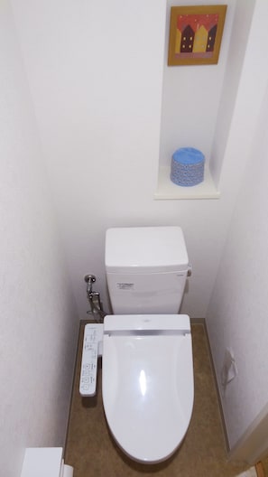 A small, compact bathroom with a white toilet, a blue toilet paper holder, and a wall-mounted shelf with a blue object. - Family Lodge Hatagoya Kochi (Kochi)