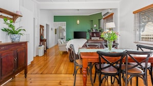 Une pièce avec un plancher en bois, une table à manger avec des chaises, un téléviseur, un lit et un mur d’accent de couleur verte.