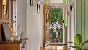Un couloir avec une porte en bois, une porte en verre avec un portail en métal, et une plante sur la droite.
