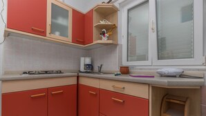 Een keuken met rode kastjes, een koffiezetapparaat en een raam met zonwering.