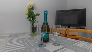 Een tafel met champagne, twee glazen, een bloemenvaas en een televisietoestel op een standaard.