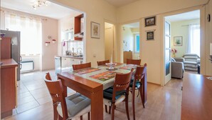 A dining area with a wooden table and chairs, a chandelier, and a kitchen in the background. - Vera Seaview Apartment (Zadar)