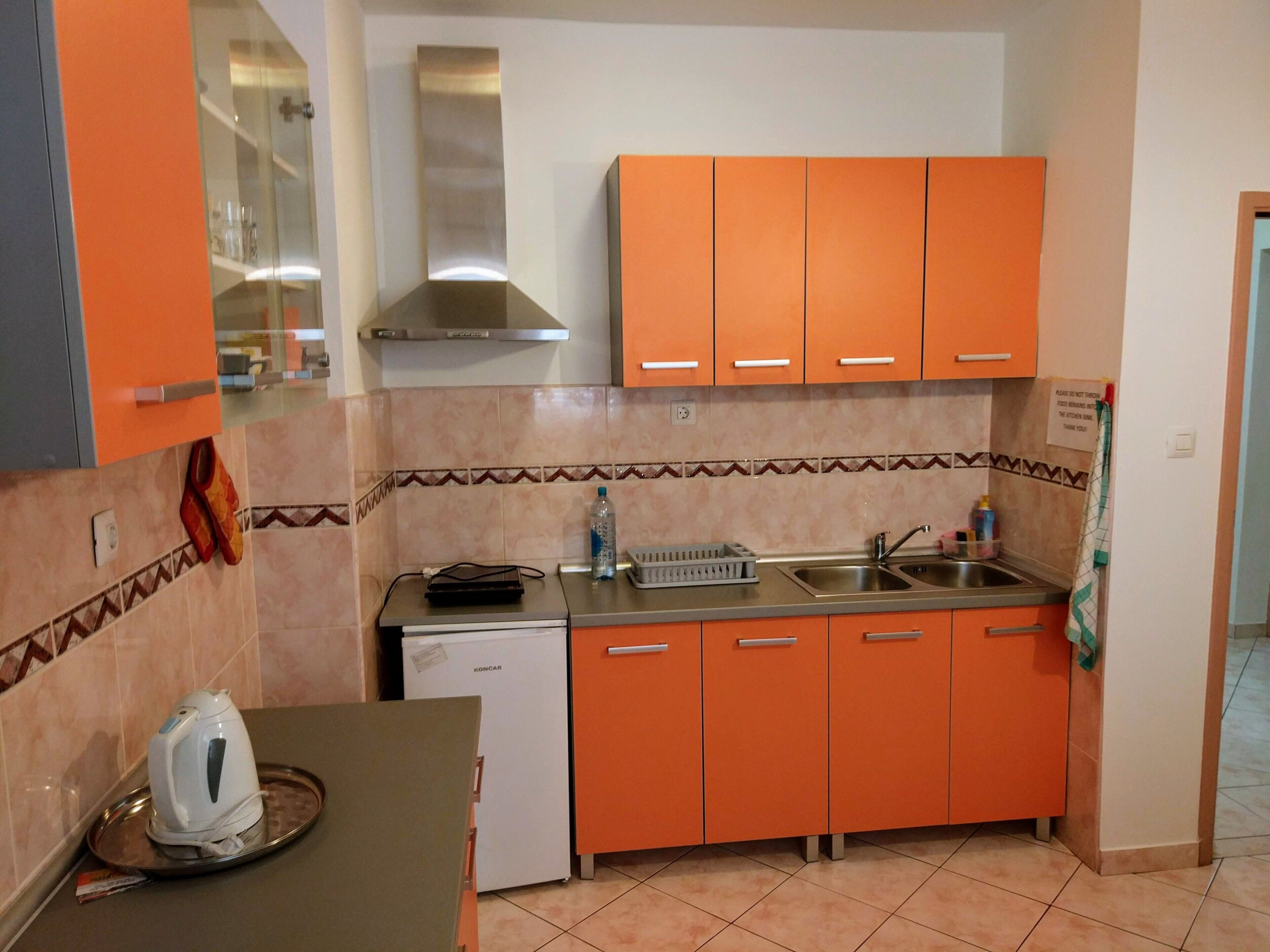 A compact kitchen with orange cabinets, a stainless steel sink, and a Koncar refrigerator.
