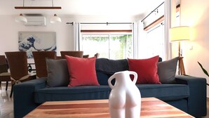 A living room with a blue sofa, red and grey cushions, a wooden coffee table, and a white vase.