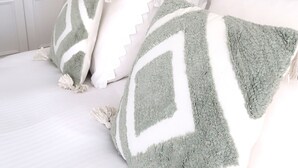 A bedroom with a bed, pillows, a headboard, a wall-mounted light, and a door.