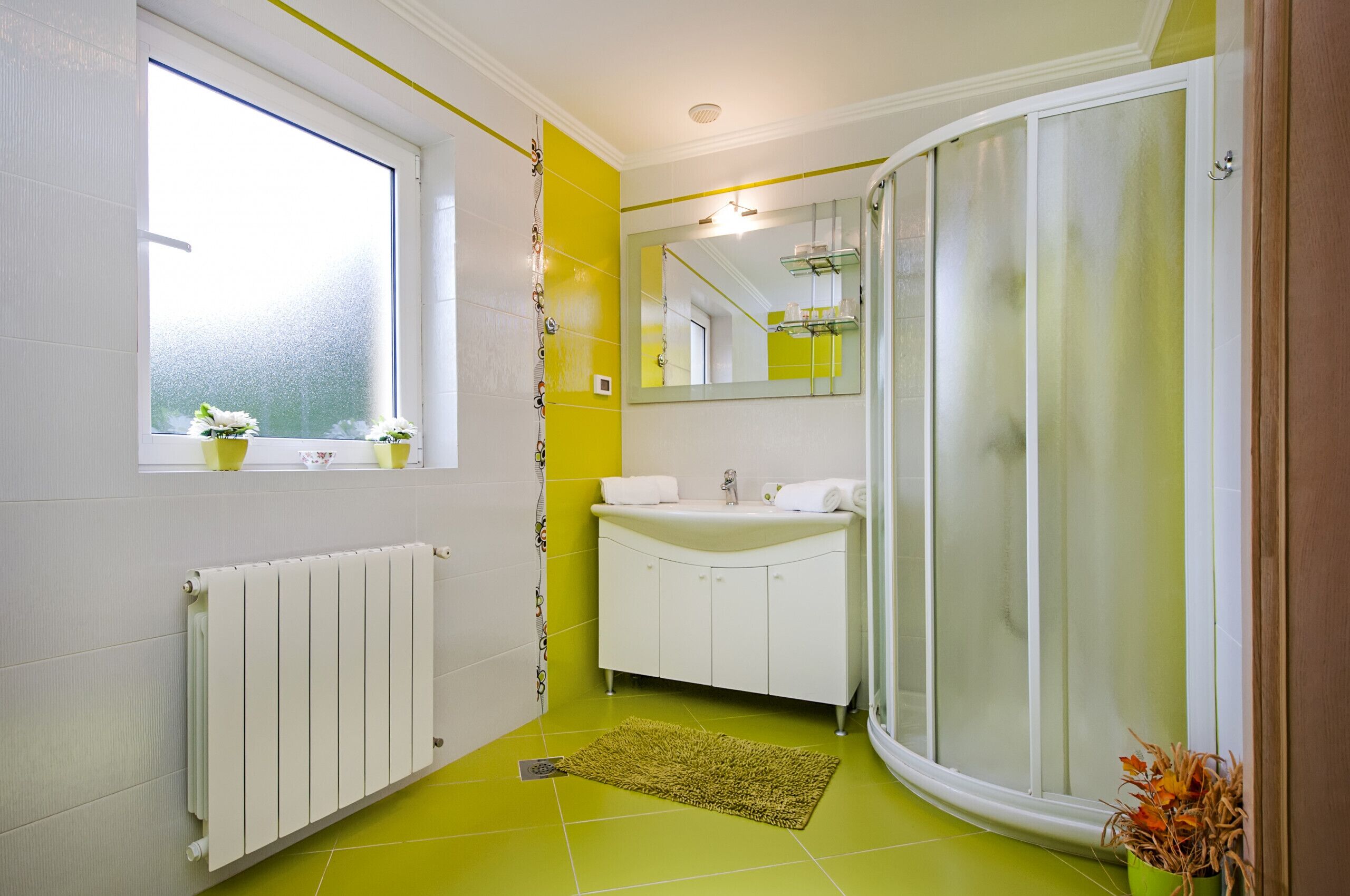 A bathroom with a window, white sink, and a shower with a glass door.