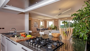 A modern kitchen with a central island, stainless steel appliances, and a dining area with a view. - Villa Montericco (Rovinj)